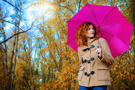Romantic dreamy girl with beautiful red hair walks in autumn park. The mood of autumn, leaf fall. Autumn fashion.の写真素材