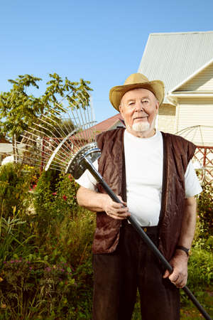 Raking in the garden. Happy senior man gardening in retirement.の写真素材
