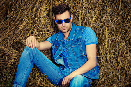 Handsome young man lying in haystack. Male fashion. Denim style.の写真素材