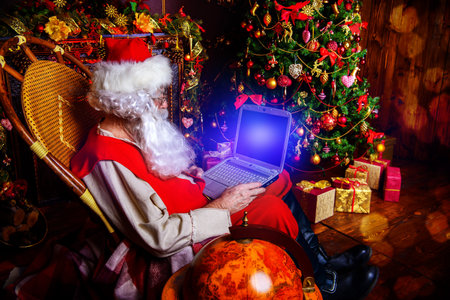 Traditional Santa Claus at his house surfing in the Internet with his laptop. Christmas time....