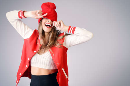 Cool cheerful girl with bright red lips wears modern knitted cap and sport jacket. Hipster style. Youth fashion.の写真素材