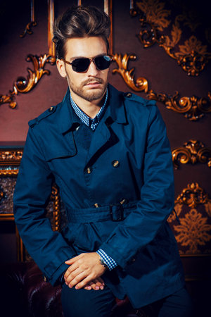 Portrait of a well-dressed imposing man in sunglasses standing in apartments with luxurious classic interior. Men's beauty, fashion. Hair styling, barbershop.の写真素材