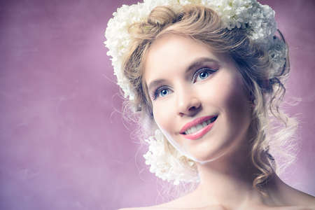 Beautiful young woman with natural make-up and wreath of white flowers on her head smiling at camera. Pink background. Summer, spring inspiration. Beauty, fashion, cosmetics.の写真素材