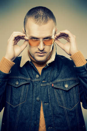 Sexual male model posing in jeans clothes and yellow sunglasses. Short hair styling. Studio fashion shot.の写真素材