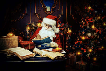 Santa Claus makes a list of gifts, sitting at home by the fireplace and Christmas tree. Christmas scene. The time of miracles.の写真素材