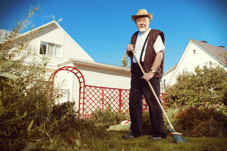 Raking in the garden. Happy senior man gardening in retirement.の写真素材