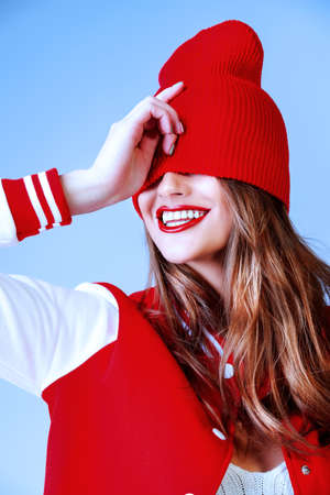 Cool cheerful girl with bright red lips wears modern knitted cap and sport jacket. Hipster style. Youth fashion.の写真素材