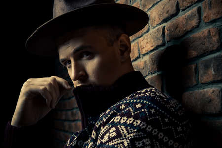 Portrait of a handsome man wearing sweater and hat standing by the brick wall. Male beauty, fashion.の写真素材