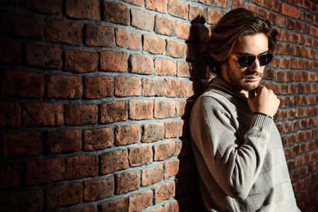 Elegant handsome young man wearing pullover and jeans standing by the brick wall. Men's beauty, fashion. Men's barbershop, Hairstyle.の写真素材