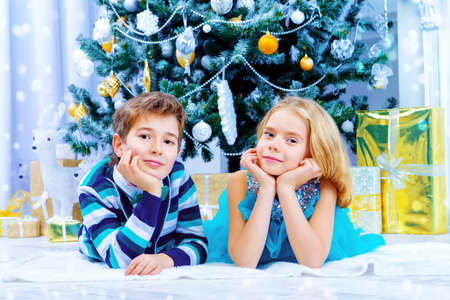 Christmas, fashion concept. Two beautiful children in elegant evening clothes posing by the Christmas tree. Classic luxurious interior decorated for Christmas.の写真素材