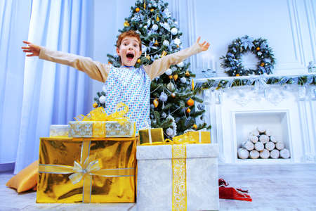 Funny boy in pajama expressing big surprise sitting near the Christmas tree and Christmas gifts. Time for miracles.の写真素材