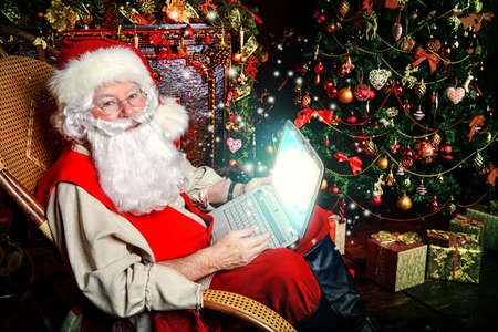 Traditional Santa Claus at his house surfing in the Internet with his laptop. Christmas time. Christmas decoration.の写真素材