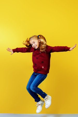 Joyful little girl jumping over yellow background. Happiness, activity and child concept. Copy...