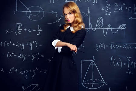Pretty student girl in strict black dress standing by a black school board. Beauty, fashion. Education, college.の写真素材