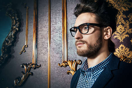 Portrait of a well-dressed imposing man in elegant glasses posing in apartments with luxurious classic interior. Men's beauty, fashion. Hair styling, barbershop.の写真素材