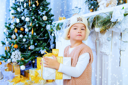 Christmas, fashion concept. Cute little boy in winter clothes posing in a room with snowy white Christmas decoration.の写真素材