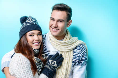 Winter, christmas and love concept. Happy man and woman in sweaters, hat and scarf hugging and smiling to each other. Winter fashion.の写真素材