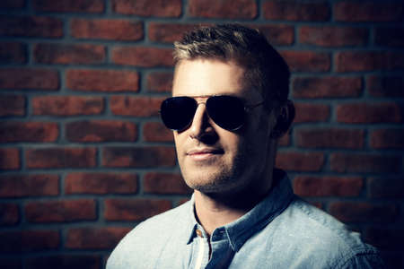 Portrait of a handsome mature man in sunglasses over brick wall background. Men's beauty, fashion.の写真素材