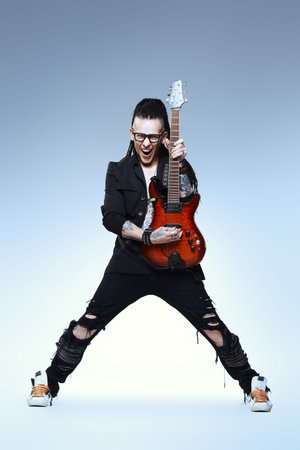 Excited rock musician is playing electrical guitar. Full length studio shot. Entertainment and...