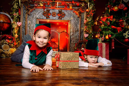Santa Claus's helpers. Two cute children in christmas elf costumes in a room beautifully decorated for Christmas. Time of miracles. Gifts from Santa Claus.の写真素材