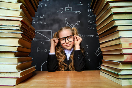 Portrait of a smart schoolgirl in glasses posing with books over school blackboard. Educational...