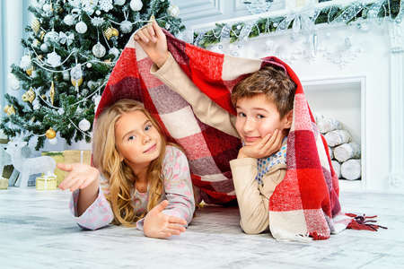 Happy funny children in pajamas playing near the Christmas tree and Christmas gifts. Luxurious Christmas decoration.の写真素材