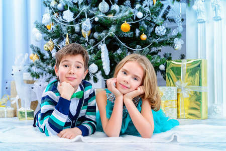 Christmas, fashion concept. Two beautiful children in elegant evening clothes posing by the Christmas tree. Classic luxurious interior decorated for Christmas.の写真素材