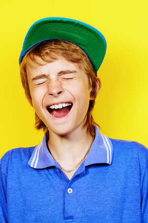 Portrait of a shouting teenage boy over yellow background. Studio shot. Teenager awkward age.の写真素材