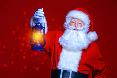 Christmas concept. Portrait of a fairytale Santa Claus holding lantern over red background. Magic time. Copy space.の写真素材