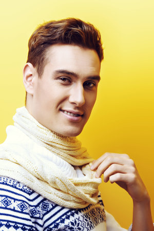 Happy young man in a sweater and a scarf looking at camera and smiling. Winter fashion. Studio shot.の写真素材