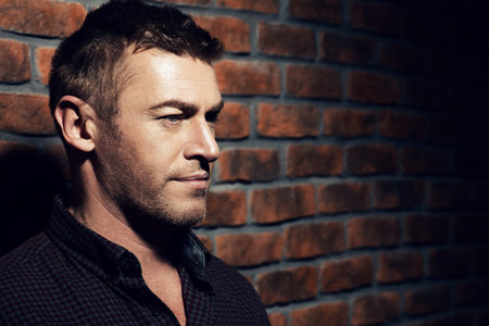 Portrait of a handsome mature man standing by the brick wall. Men's beauty, fashion.