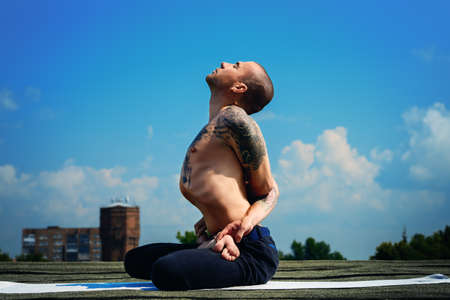 Yoga concept. Experienced yoga master meditates in the lotus position sitting on a roof over blue sky.の写真素材