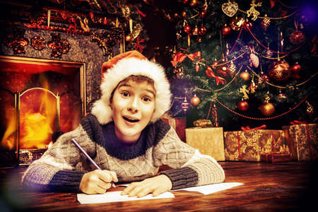 Happy joyful boy in Santa's hat writing a letter to Santa Claus. Christmas concept. Belief in miracles.の写真素材