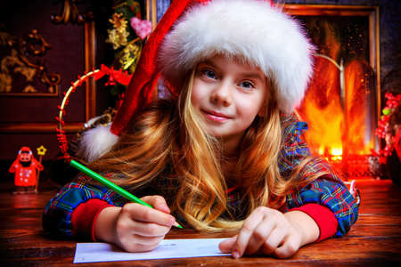 Cute girl in Santa's hat writing a letter to Santa Claus. Christmas concept. Belief in miracles.の写真素材