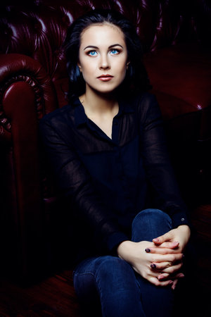 Beautiful dreamy girl sitting on a floor by a sofa. Beauty, fashion. Natural make-up, cosmetics.