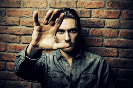 Brutal man holds his hand to the camera. Brick wall background. Stop sign.の写真素材