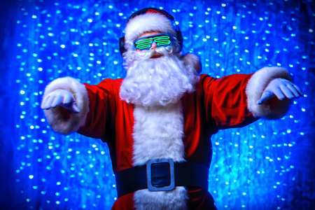 DJ Santa Claus in luminous glasses and headphones. Christmas songs and music. Disco lights in the background.の写真素材