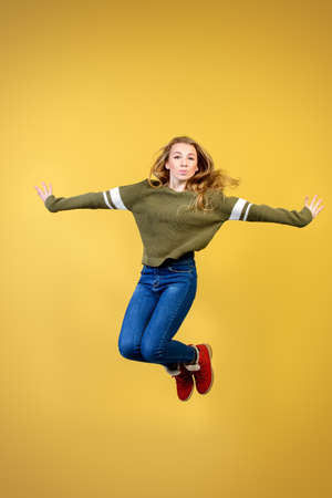Joyful teen girl jumping over yellow background. Happiness, activity and child concept. Copy space.の写真素材