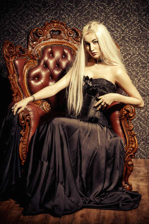 Gothic style. Beautiful young woman with long blonde hair and black make-up wearing long black dress. Vintage interior, castle style. Halloween.の写真素材
