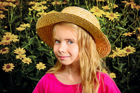 Portrait of a cute dreamy girl in a straw hat standing in a summer blooming park and smiling at camera. Happy childhood. Summer holidays.の写真素材