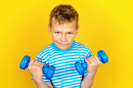 Portrait of a boy with dumbbells over yellow background. Healthy lifestyle. Sports and activities for children.の写真素材