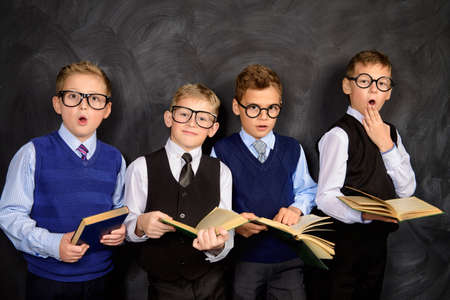 Group of smart boys in formal suits and spectacles standing with books by a blackboard. Educational concept. Copy space.の写真素材