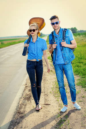 Hitchhiking couple. Romantic young people standing on a highway and catching a passing car.の写真素材