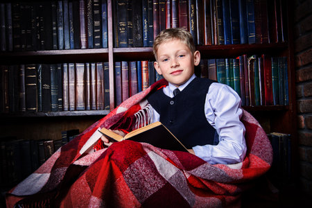 Smart boy in a suit sitting in the library by the bookshelves with many old books. Educational concept. Science.の写真素材