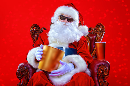 Merry Christmas and Happy New Year. Santa Claus sitting on his armchair and eating popcorn and...