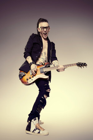 Excited rock musician is playing electrical guitar. Full length studio shot. Entertainment and...