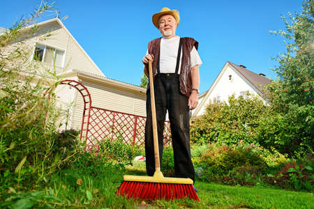 Raking in the garden. Happy senior man gardening in retirement.の写真素材