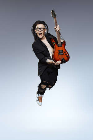 Entertainment and musical concept. Excited rock musician is jumping with his electrical guitar. Full length studio shot.の写真素材