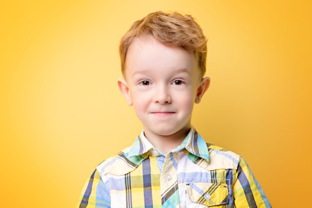 Portrait of a cute little boy looking at camera and smiling. Yellow background. Copy space. Children...