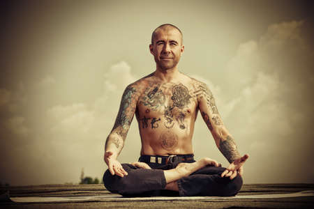 Yoga concept. Experienced yoga master meditates in the lotus position sitting on a roof over blue sky.の写真素材